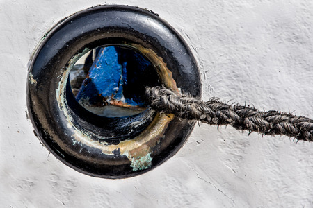 Close up view of black porthole on the iron white fisherman boat with black rope exiting on the right side.の写真素材