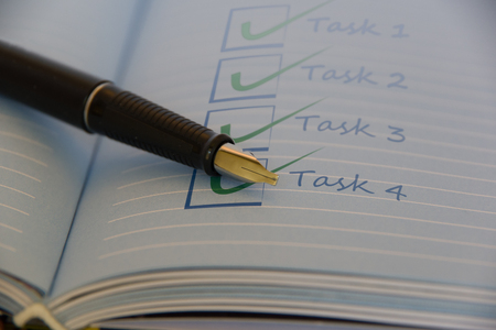 Close up view of an open notebook with completed checklist and one black fountain pen on the left side.の写真素材