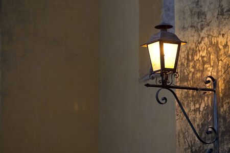 A spanish style lamp mounted to a concrete wall glows in the eveningの写真素材