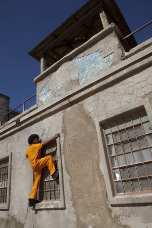 An african american male in orange prison coveralls escapes from prison by climbing a wallの写真素材