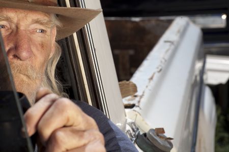 An elderly man with a white beard driving a pickup truck and staring out the window