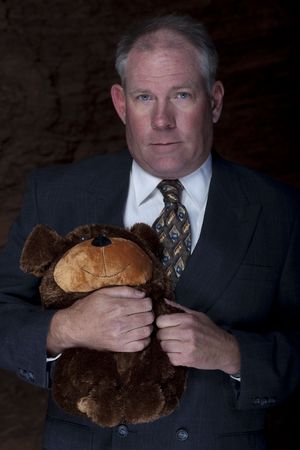 A businessman is clutches on to a teddy bear for security with a dark and rocky landscape in the background. Vertical shot.の写真素材