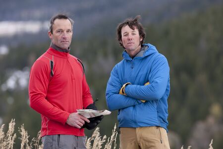 Two men stand together in the wilderness and look at the camera with serious expressions. One is holding a map. Horizontal format.の写真素材