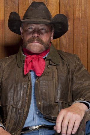 Portrait of a cowboy with a mustache in front of a rough wood wall. He is staring at the camera with a serious expression. Vertical format.の写真素材
