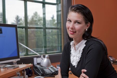 Portrait of a businesswoman sitting at a computer in her office. She is resting on her elbows and smiling at the camera. Horizontal format.の写真素材