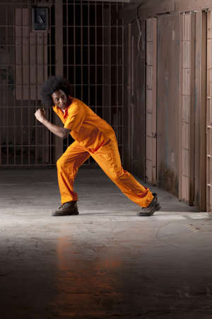 A young african american man with an afro is looking behind him as he is making an escape from a prison cell. Vertical shot.の写真素材