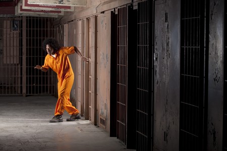 A young african american man with an afro is sneaking out of a prison cell. Vertical shot.の写真素材