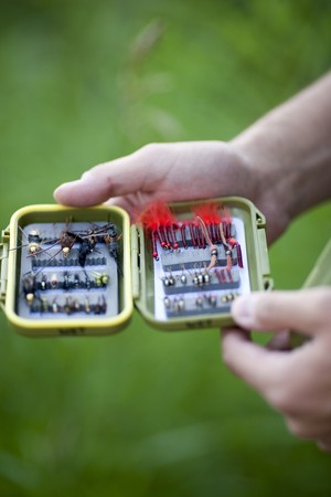 A pair of male hands is holding an open box of flies for fly fishing. Vertical shot.の写真素材