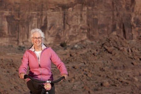 A senior woman is smiling as she rides her bike in a desert setting. Horizontal shot.の写真素材