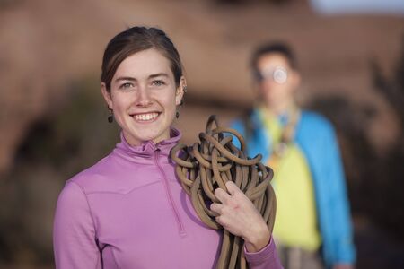 An attractive young woman is holding a rope used for mountain climbing. Her partner can be seen in the background. Vertical shot.の写真素材