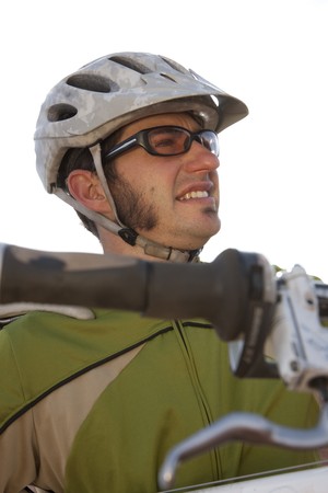 A young man wearing protective eyewear and a helmet is carrying a mountain bike. Vertical shot.の写真素材