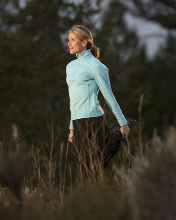 An attractive young woman is wearing athletic clothing and stretching before jogging. She is smiling and facing the sun. Vertical shot.の写真素材