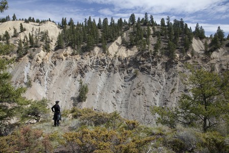 A woman is standing at the edge of a cliff, looking out across a canyon. Horizontal shot.の写真素材