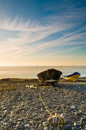 Two small boats moored up on a shingle beach at sunrise.の写真素材