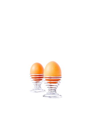 Boiled eggs in metal wire eggcups isolated against a white background.の写真素材