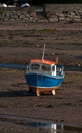 A small fishing boat stranded on the beach at low tide.の写真素材