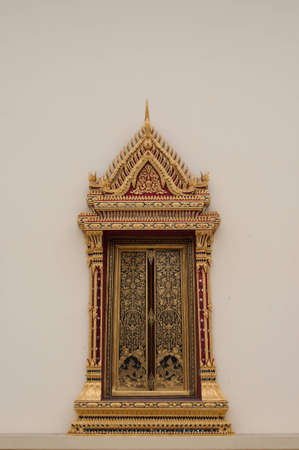 The arched window of a thai church which was made by hand using gold leaf, lacquer, colored glass mosaic and brassの写真素材