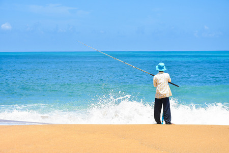 Fisherman fishing at the beach and wave of the sea, blue sky with fishing rod Fisherman fishing at the beautiful seascape Man fishing on Beach.の写真素材