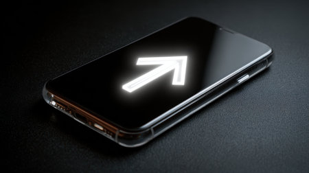 Modern smartphone on dark surface displaying glowing upward arrow symbol representing growth, progress, and direction in technology and communicationの素材