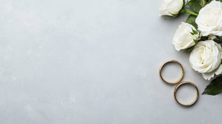 Elegant wedding composition with white roses and golden rings on textured grey surface, perfect for love, romance, and engagement themes.の素材