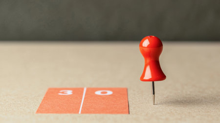 Close-Up View of a Red Pushpin on a Table Next to a Numbered Card Displaying the Number 30 for Office or School Useの素材