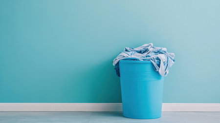 Blue Plastic Bucket Filled with Dirty Laundry Stands Against a Mint Green Wall in a Bright and Cheerful Room Settingの素材
