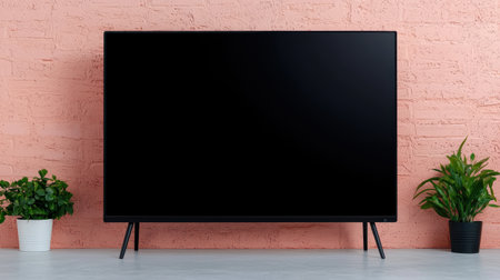 Modern minimalist interior with a blank television screen on a stylish stand against a pink brick wall with potted plants for contemporary decor inspirationの素材