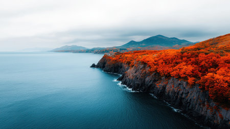 Scenic Coastal Landscape with Vibrant Orange Foliage, Calm Blue Waters, and Majestic Mountains Under a Cloudy Sky in Autumn Atmosphereの素材