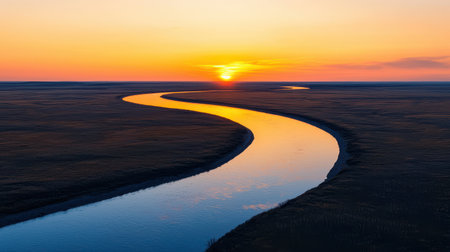 A serene sunset over a winding river, reflecting warm hues on tranquil waters amidst an expansive landscape.の素材