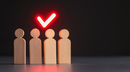 Wooden figures with one highlighted by a glowing red check mark, symbolizing approval, success, and achievement against a dark backgroundの素材