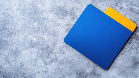A vibrant blue and yellow folder rests on a textured gray surface, showcasing a minimalist design ideal for organizing documents.の素材