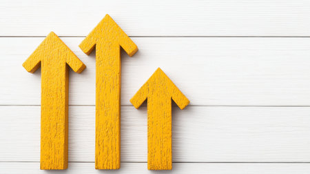 Three upward-pointing yellow arrows symbolize growth and progress on a white wooden background.の素材
