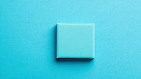 A single turquoise square tile rests on a matching turquoise background, creating a minimalist and modern aesthetic.の素材