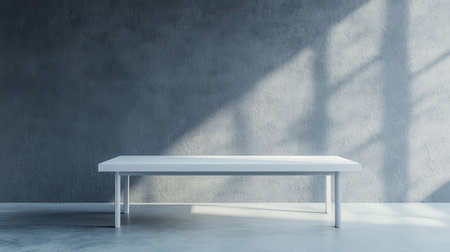 A minimalist white table sits against a textured gray wall, illuminated by soft shadows, creating a serene and modern atmosphere.の素材