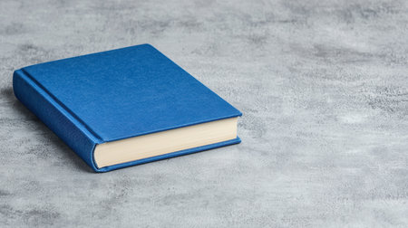 A blue hardcover book lies on a textured gray surface, showcasing its simple elegance and inviting readers to explore its contents.の素材