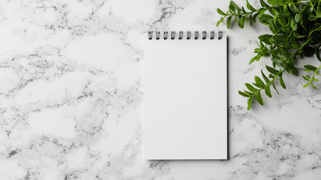 Empty Spiral Notepad with Blank Pages on Marble Surface Surrounded by Fresh Green Foliage for Creative Inspiration or Planning Purposeの素材