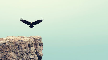 A majestic eagle soars above a rocky cliff, showcasing its powerful wings against a soft, muted background.の素材