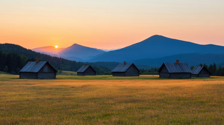 A serene landscape featuring wooden cabins at sunset, with rolling hills and mountains in the background, bathed in warm hues.の素材