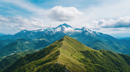 A breathtaking view of snow-capped mountains and lush green hills under a cloudy sky, showcasing the beauty of nature's landscape.の素材