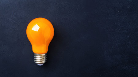 Bright Orange Light Bulb on Dark Background with Minimalistic Design for Ideas and Creativity in Home or Office Settingsの素材