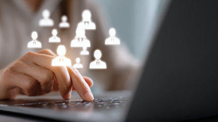 Close-up of a hand typing on a laptop keyboard with floating user icons, representing digital communication and networking in modern technology environmentsの素材