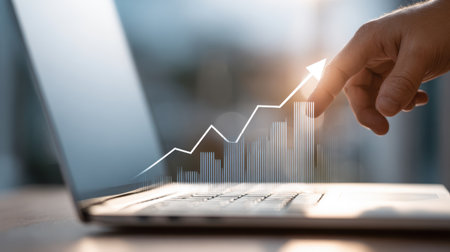 Business growth concept showcasing a hand pointing at a laptop screen with a rising graph symbolizing success and progress in the digital ageの素材