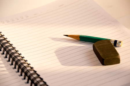 Green Pencil and black eraser placed on a notebook and sunlight