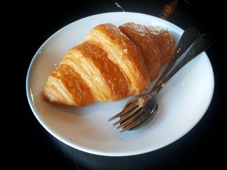 isolated plain croissant  on a white dish and utensils on black backgroundの写真素材
