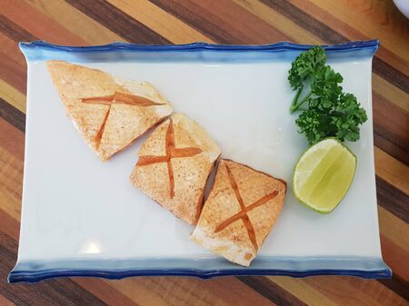 burn salmon belly cut in cross shape on served with lemon lime and japanese vegetable leaf on a white plate in japanese styleの写真素材