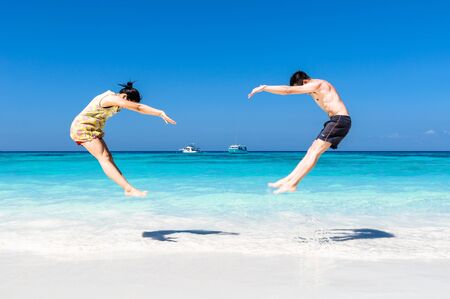 The happy Cheerful couple enjoys relaxing and jumping at white sand beach with blue sky and blue sea background.の写真素材