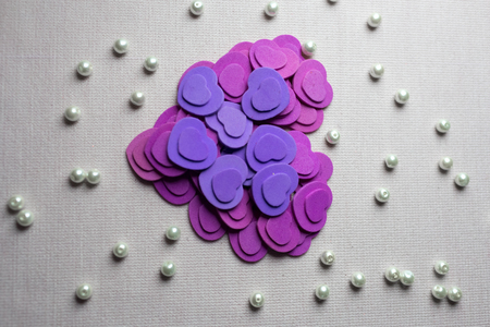 Purple hearts and pearls lying on a beige fabric.の写真素材