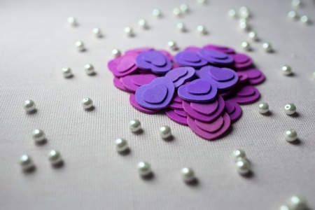 Purple hearts and pearls lying on a beige fabric.の写真素材