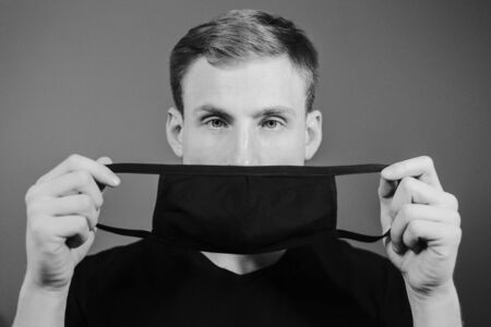 Handsome man in black t-shirt wear black medical mask, gray background. Coronavirus covid-19...