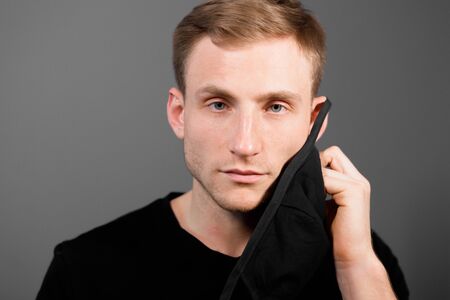 Handsome man in black t-shirt wear black medical mask, gray background. Coronavirus covid-19...